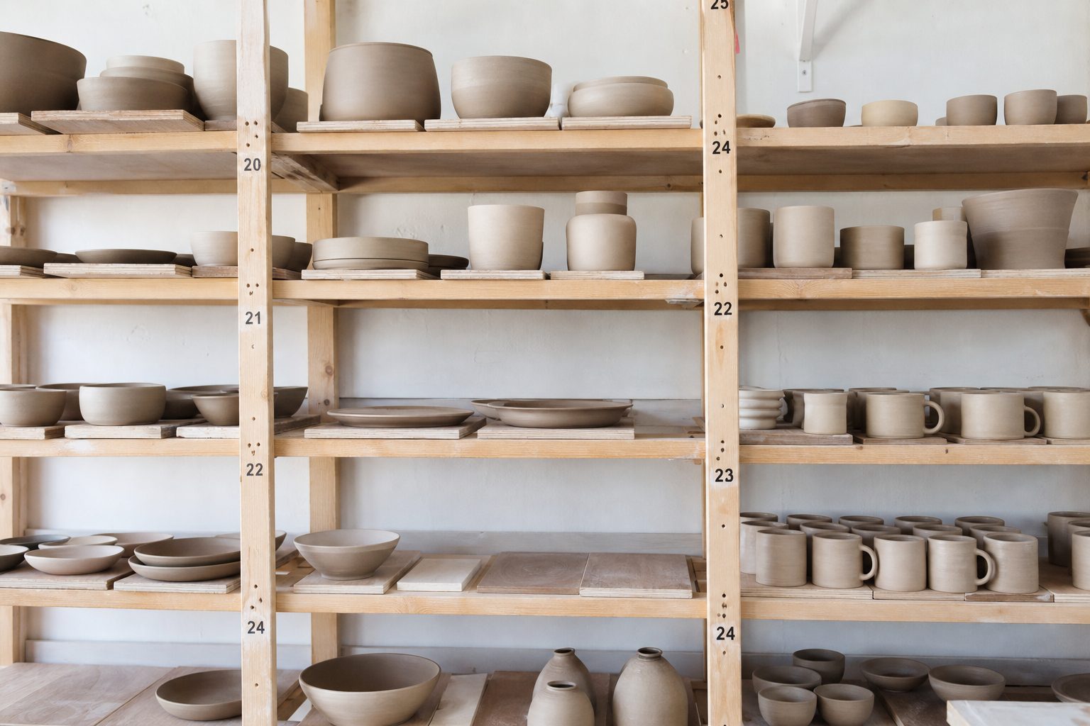 Numbered wooden studio shelves holding greenware and bisque pots in daylight